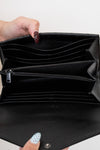 Black wallet held open by a hand with painted nails on a white background