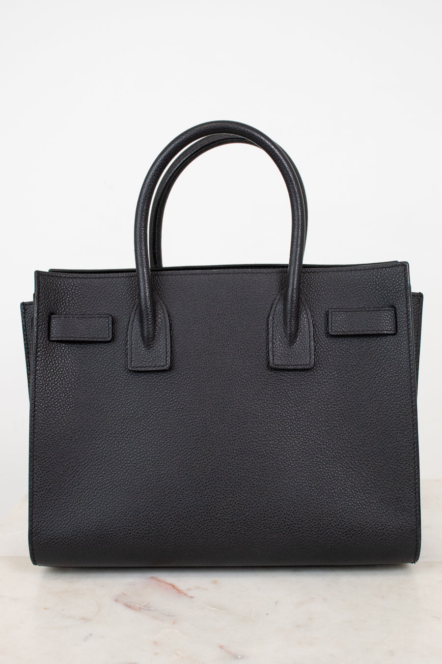 A black pebbled leather handbag with double top handles, shown against a clean white background.