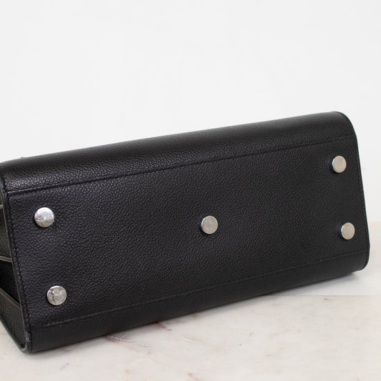 A black pebbled leather long wallet or clutch with silver-tone metal studs, resting on a white marble surface against a white background.