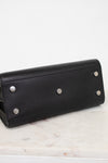 A black pebbled leather long wallet or clutch with silver-tone metal studs, resting on a white marble surface against a white background.