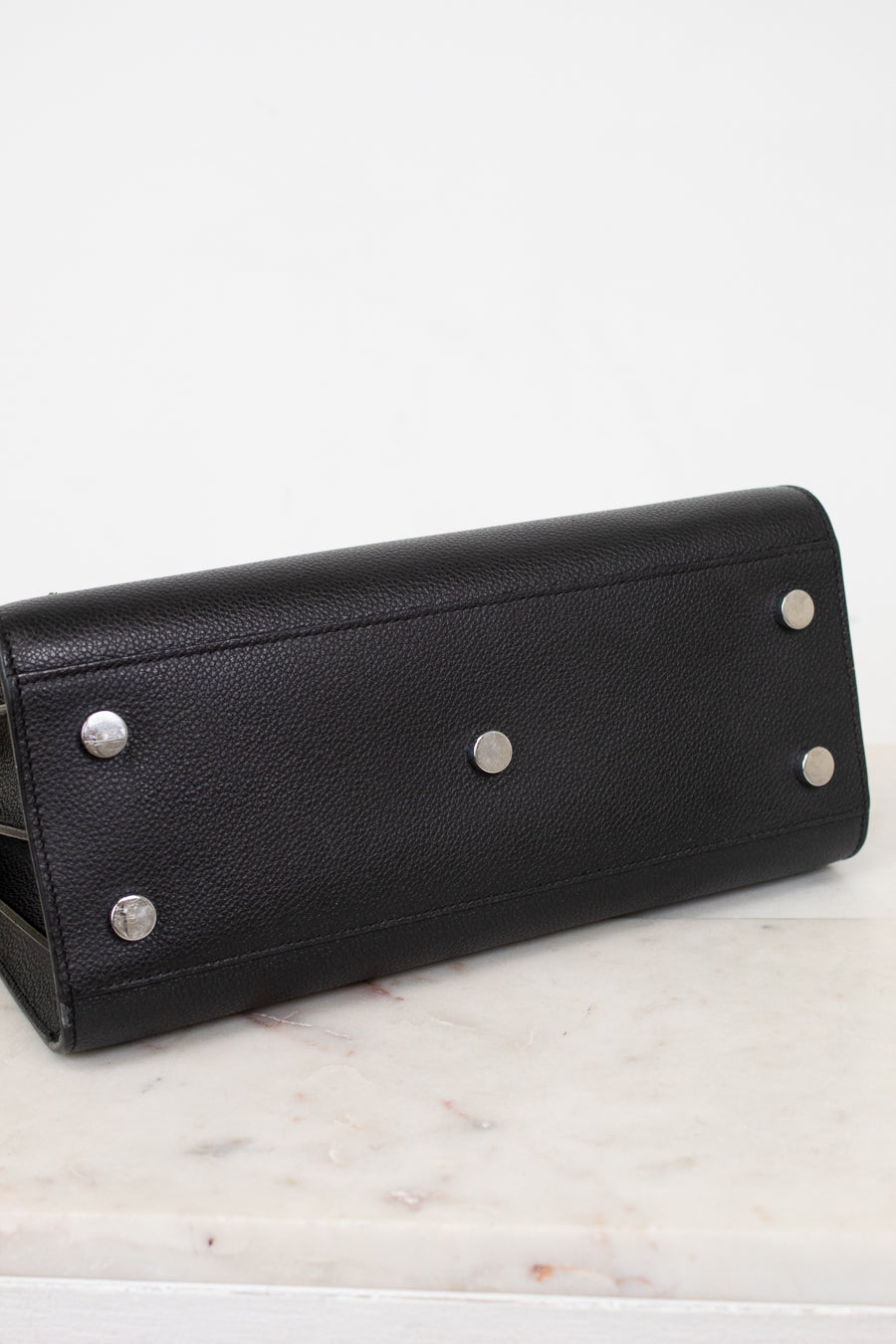 A black pebbled leather long wallet or clutch with silver-tone metal studs, resting on a white marble surface against a white background.