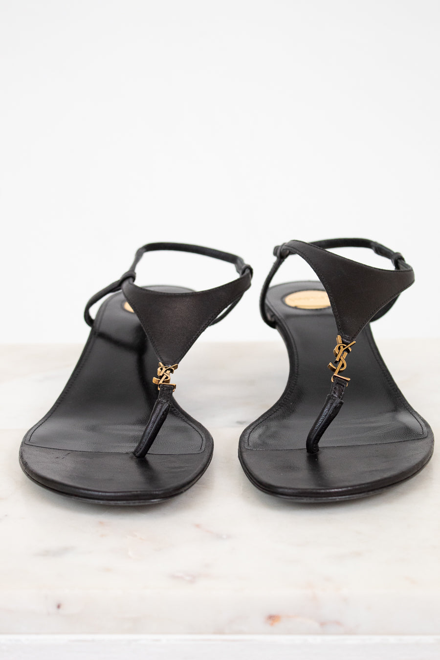 Pair of black sandals with a "YSL" brand logo on a light background