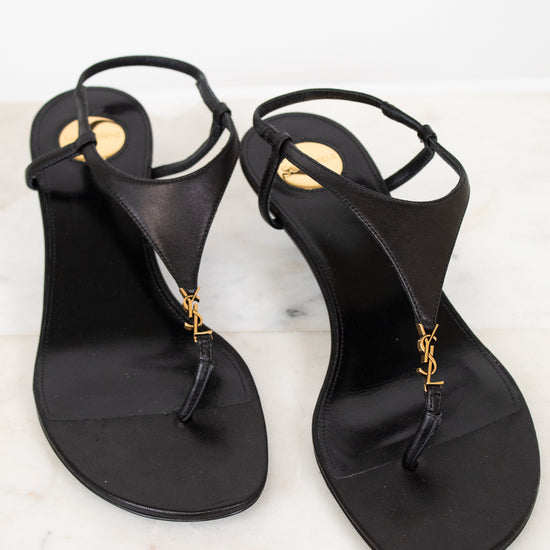 Pair of black sandals with gold accents on a white marble surface