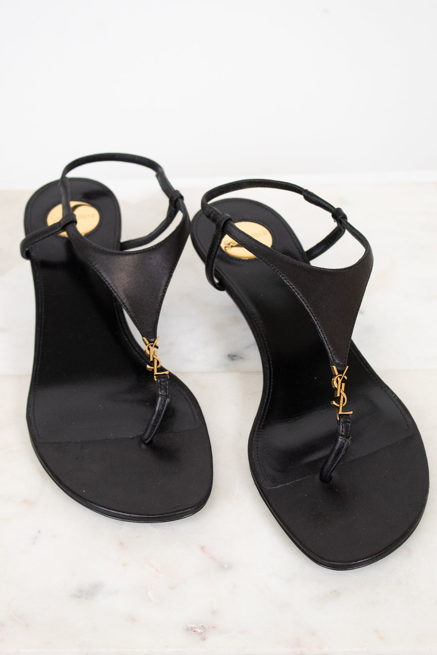Pair of black sandals with gold accents on a white marble surface