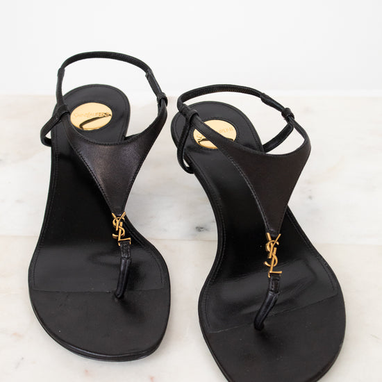 Pair of black sandals with gold accents on a light background