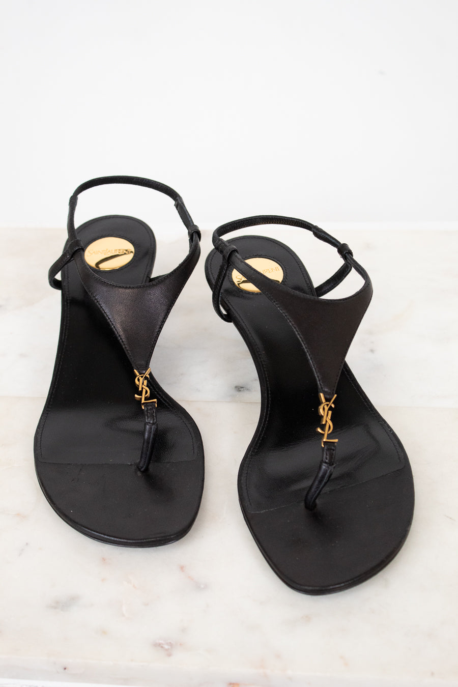 Pair of black sandals with gold accents on a light background