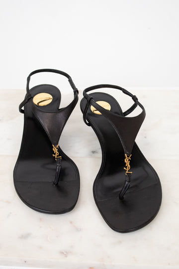 Pair of black sandals with gold accents on a light background