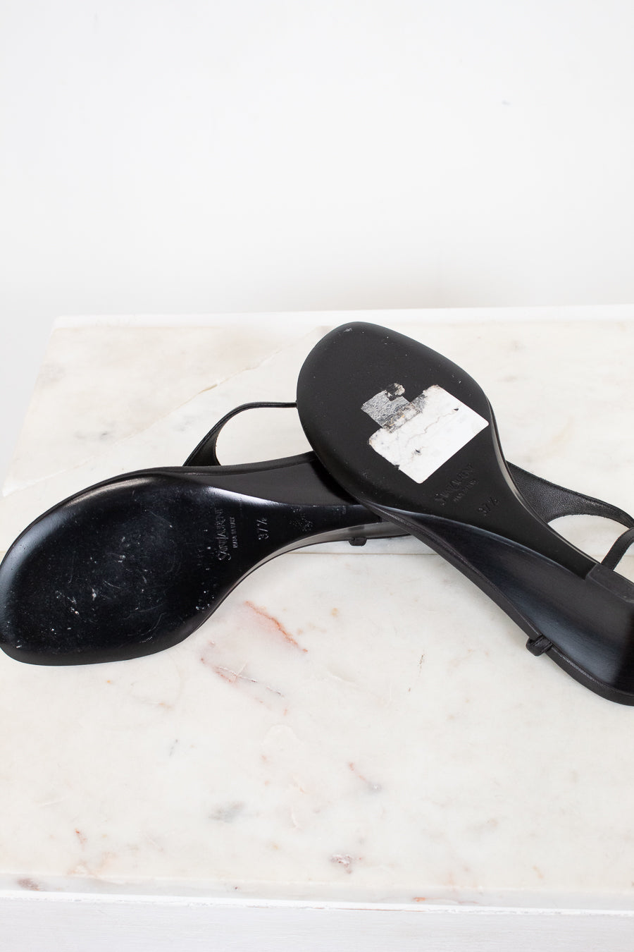 Black heeled shoes with black soles on a marble surface