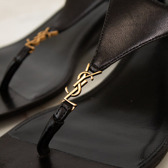 Black sandal with gold decorative strap on a light background