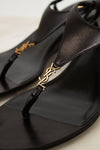 Black sandal with gold decorative strap on a light background