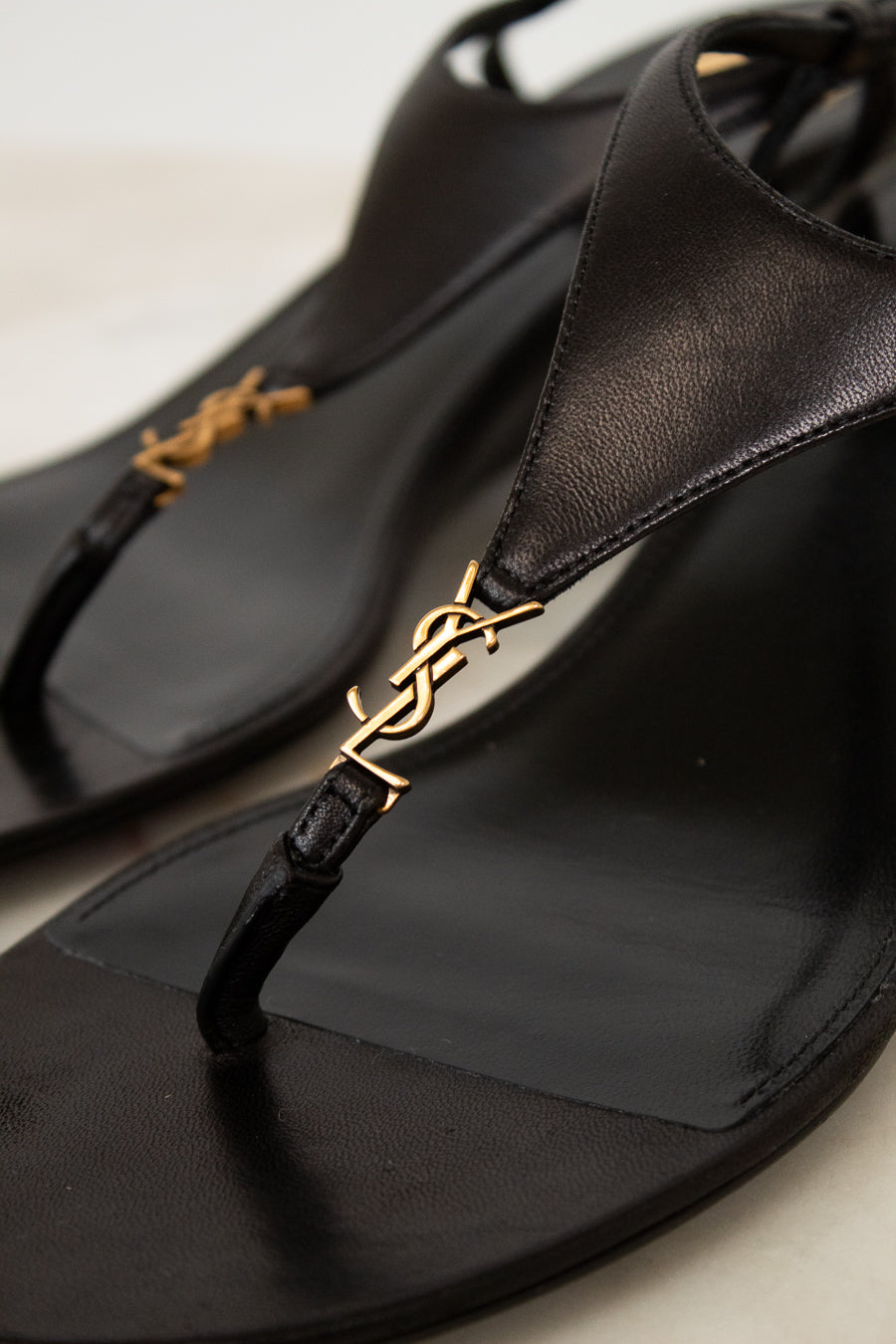 Black sandal with gold decorative strap on a light background