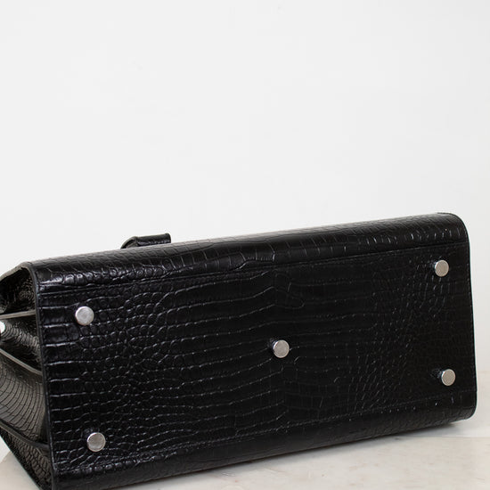 A black textured leather clutch purse with silver-tone metal studs, shown from a side angle on a light marble surface against a white background.