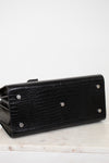 A black textured leather clutch purse with silver-tone metal studs, shown from a side angle on a light marble surface against a white background.