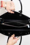 Close-up of a black leather handbag interior with a top zipper, held open by two hands against a plain light background.