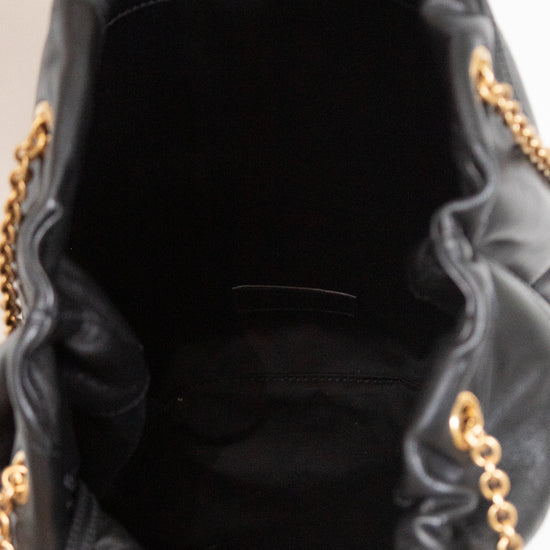 Black leather bucket bag shown from the inside, featuring a black fabric lining, a gold-tone snap button closure, and gold chain straps visible at the sides.