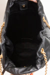 Black leather bucket bag shown from the inside, featuring a black fabric lining, a gold-tone snap button closure, and gold chain straps visible at the sides.