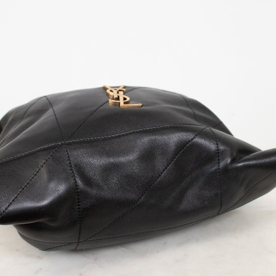 A black leather shoulder bag with a gold-tone YSL logo clasp, resting on a white marble surface against a white background.