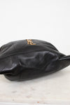 A black leather shoulder bag with a gold-tone YSL logo clasp, resting on a white marble surface against a white background.