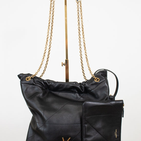 A black leather Saint Laurent shoulder bag with gold-tone chain straps and a matching black leather pouch, displayed on a white background with a stand.