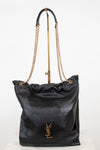A black leather shoulder bag with a gold-tone YSL hardware logo, featuring a quilted pattern, a drawstring top, and a gold chain strap, displayed on a stand against a white background.