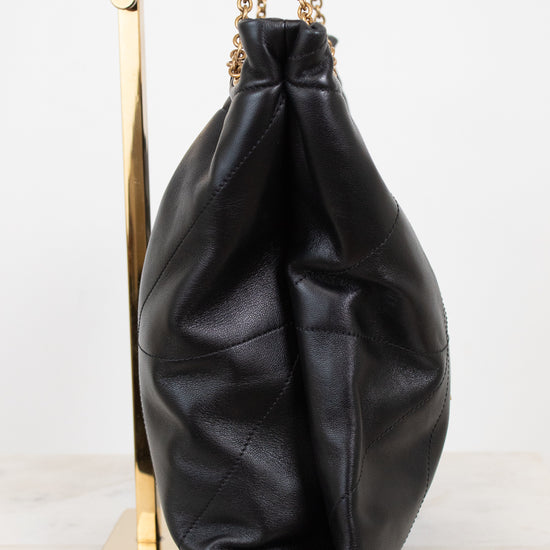 A black leather slouchy bucket bag with gold chain straps, displayed on a gold stand against a white background.