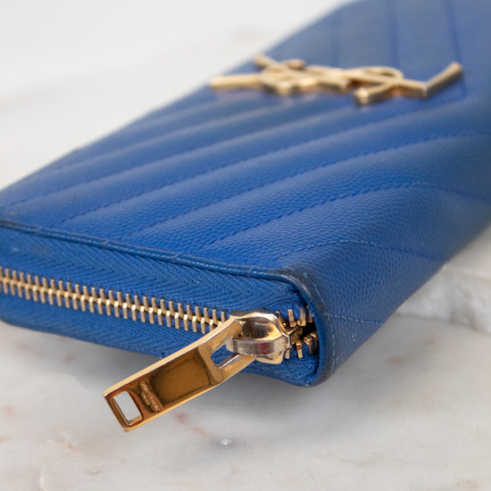 Blue wallet with gold zipper and logo on a marble surface