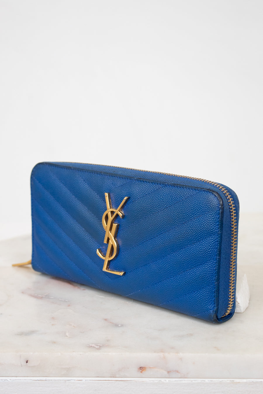 Blue wallet with gold logo on a marble surface