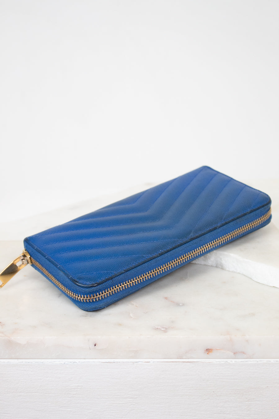 Blue wallet with gold zipper on a white marble surface