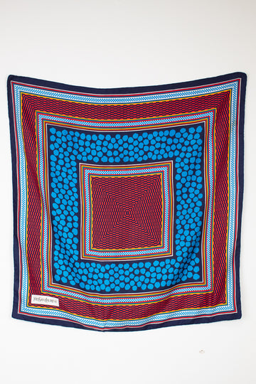 A square scarf with a vibrant geometric pattern, featuring concentric squares of blue, red, navy, and yellow on a plain white background.