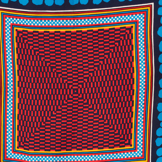 A square scarf with a bold geometric pattern, featuring a central red, black, and blue abstract checkerboard-like grid surrounded by concentric multicolor borders, with a dark navy background patterned with bright blue dots at the top and bottom.