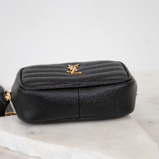A black pebbled leather pouch with a gold-tone YSL logo on the front, resting on a white marble slab against a light gray background.
