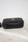 A black pebbled leather pouch with a gold-tone YSL logo on the front, resting on a white marble slab against a light gray background.