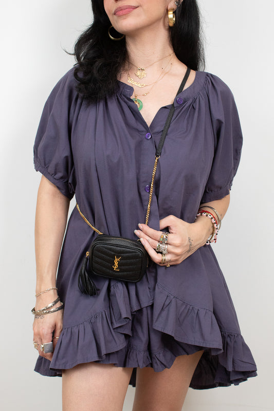 A woman wearing a short-sleeve, ruffled mini dress in a muted purple shade, styled with a black quilted crossbody bag featuring a gold chain strap and YSL monogram.