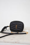 A black quilted leather crossbody bag with a gold-tone YSL monogram logo and a gold chain strap, resting on a white marble surface against a white background.