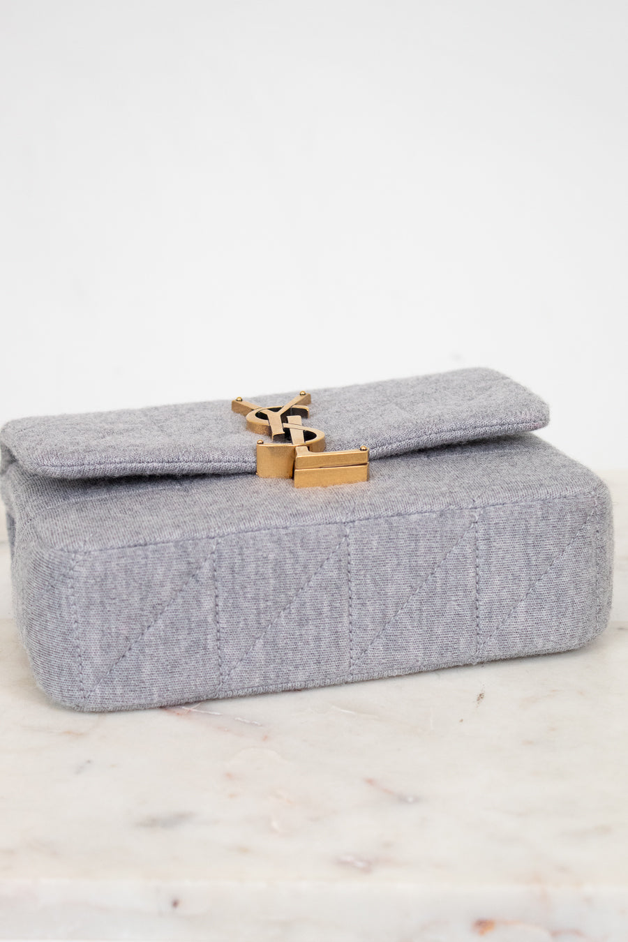 Gray YSL bag with a gold clasp on a marble surface