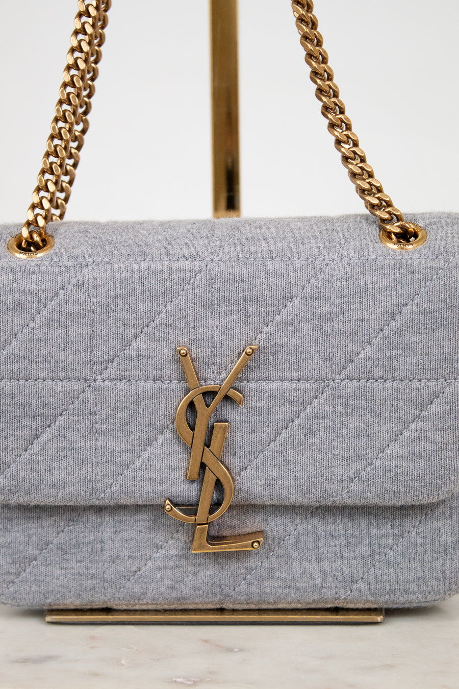 Gray quilted handbag with gold chain strap and YSL logo on a white background