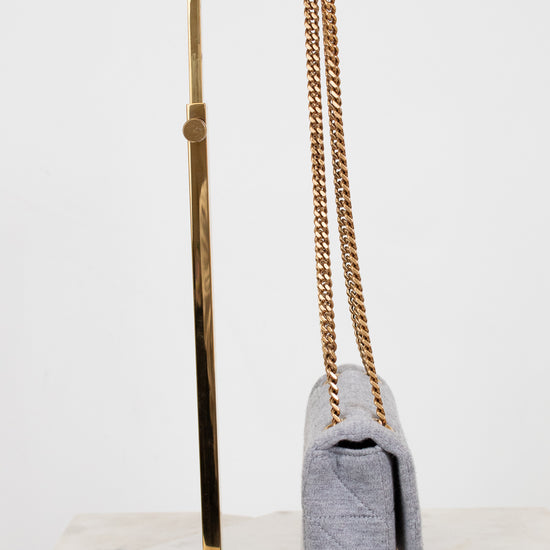 Gray handbag with gold chain on a gold stand against a white background