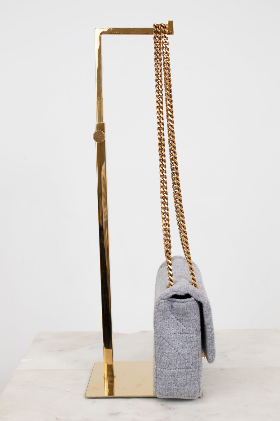 Gray handbag with gold chain on a gold stand against a white background