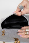 Close-up of a hand with rings opening a gray handbag with black interior