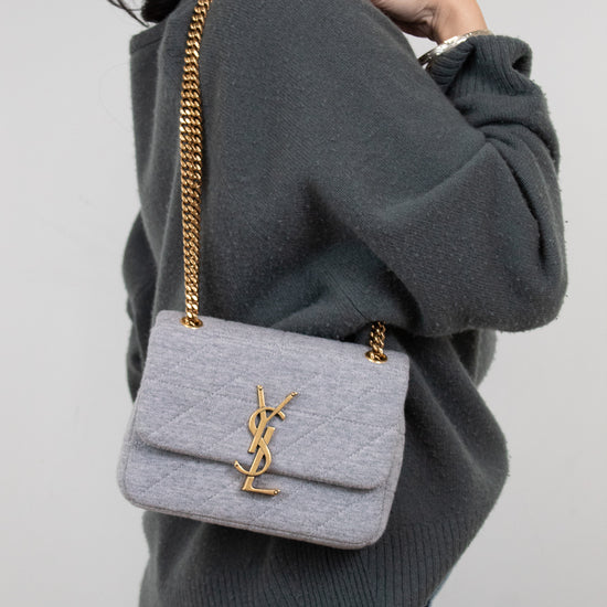 Person wearing a gray sweater with a light gray quilted YSL handbag on a plain background