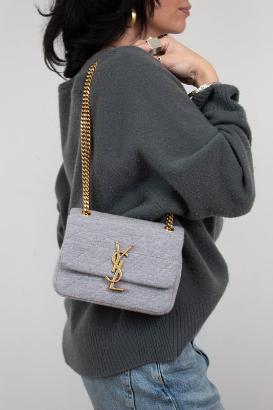 Person wearing a gray sweater with a light gray quilted YSL handbag on a plain background