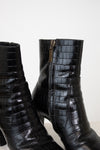 Black crocodile-embossed leather ankle boots with a side zipper and block heel, shown against a plain light background.
