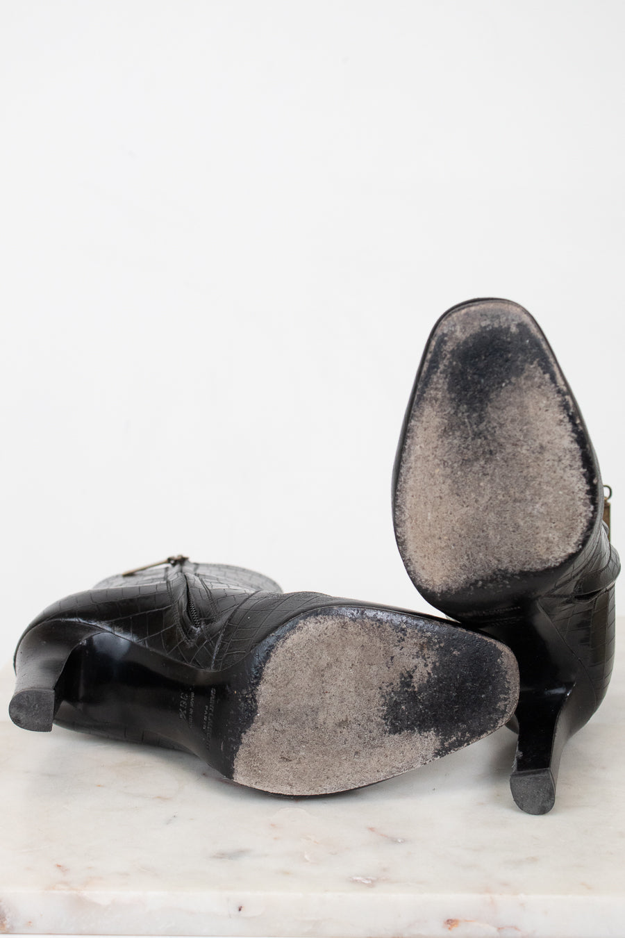 A pair of black leather high-heeled shoes shown from the bottom, revealing heavily worn bottom soles, set against a plain white background.