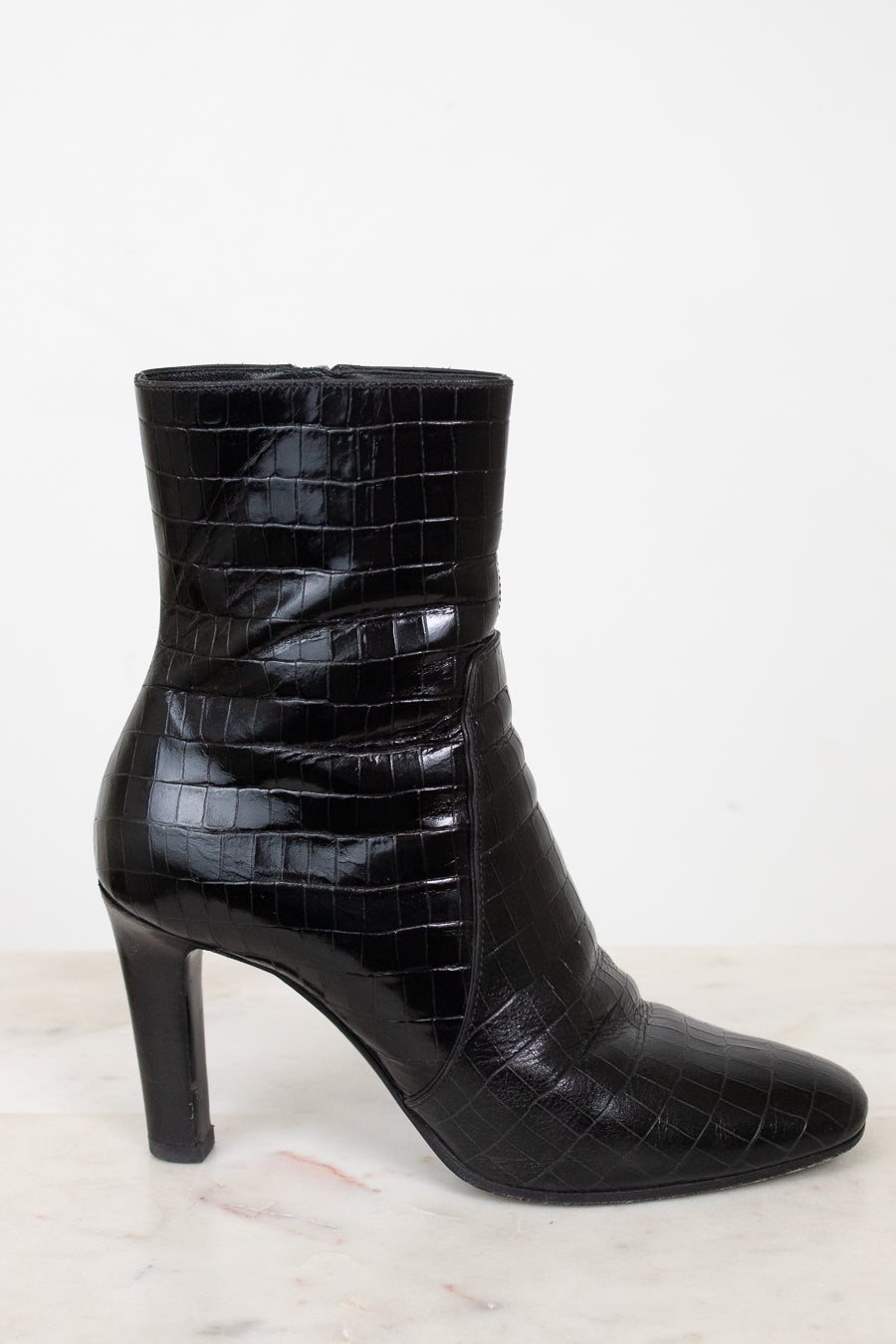 A single black ankle boot with a glossy crocodile-embossed texture and a high block heel, shown from a side profile against a white background.