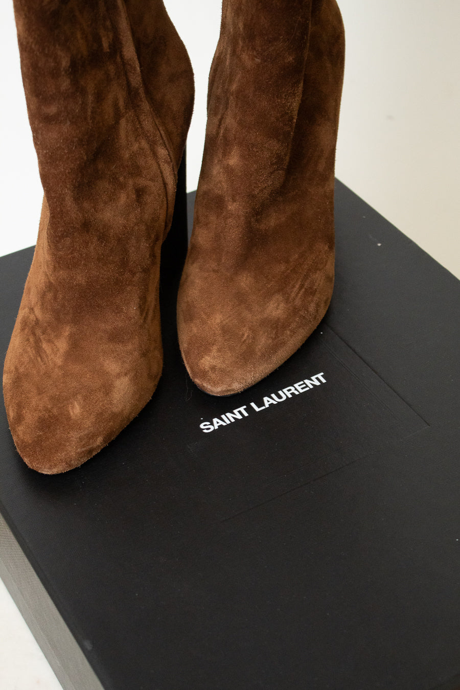 A pair of brown suede ankle boots shown sitting on a black "Saint Laurent" box