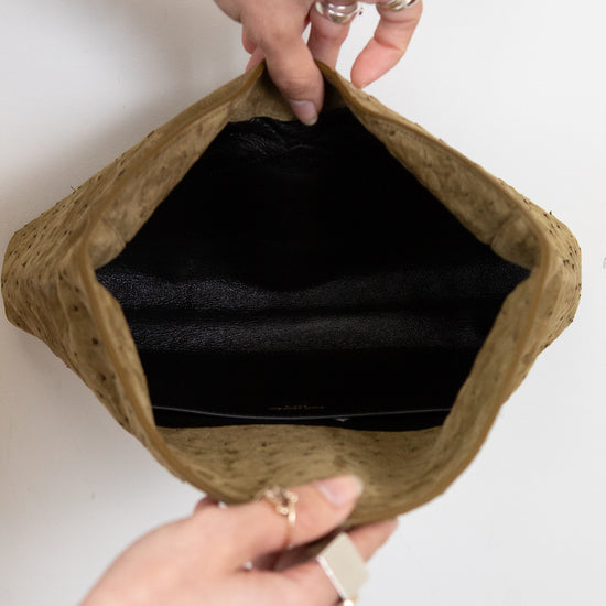 Brown clutch bag with black interior held by hands on a white background