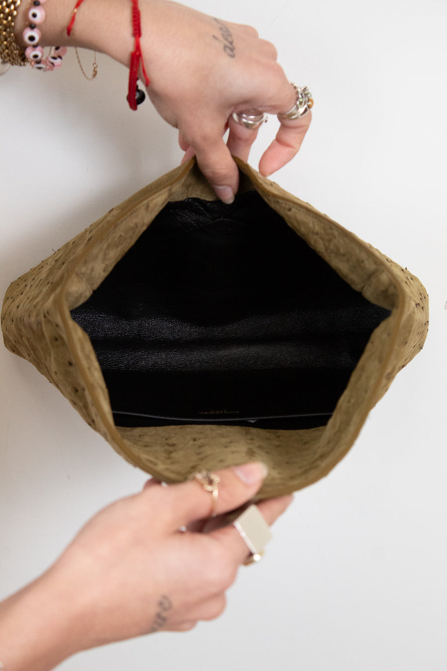 Brown clutch bag with black interior held by hands on a white background