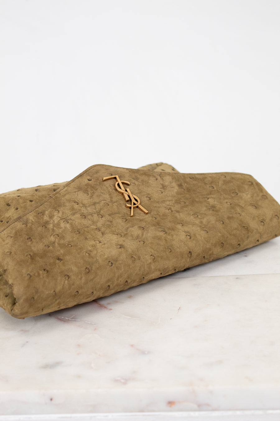 Brown textured clutch with gold YSL logo on a marble surface