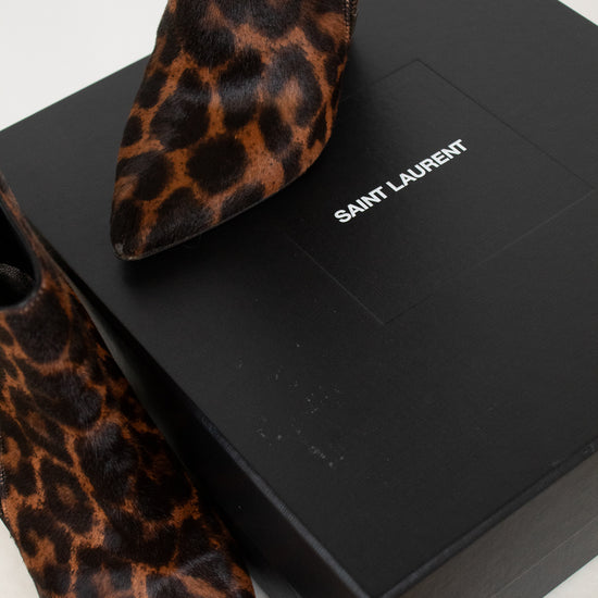 Saint Laurent leopard-print pointed-toe ankle boots displayed on a black Saint Laurent shoebox against a light marble background.