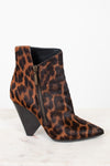 A pointed-toe ankle boot with a brown and black leopard print pattern, featuring a black conical heel and a side zipper, displayed on a light marble surface against a white background.